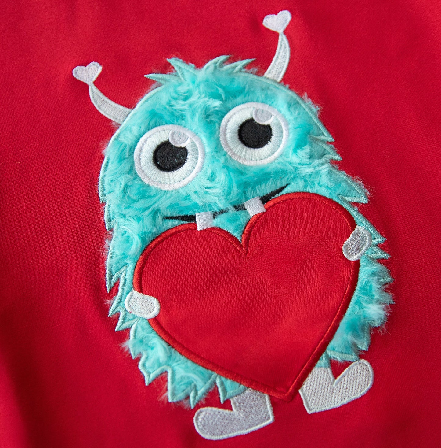 Red shirt with a turquoise monster holding a red heart on a red background