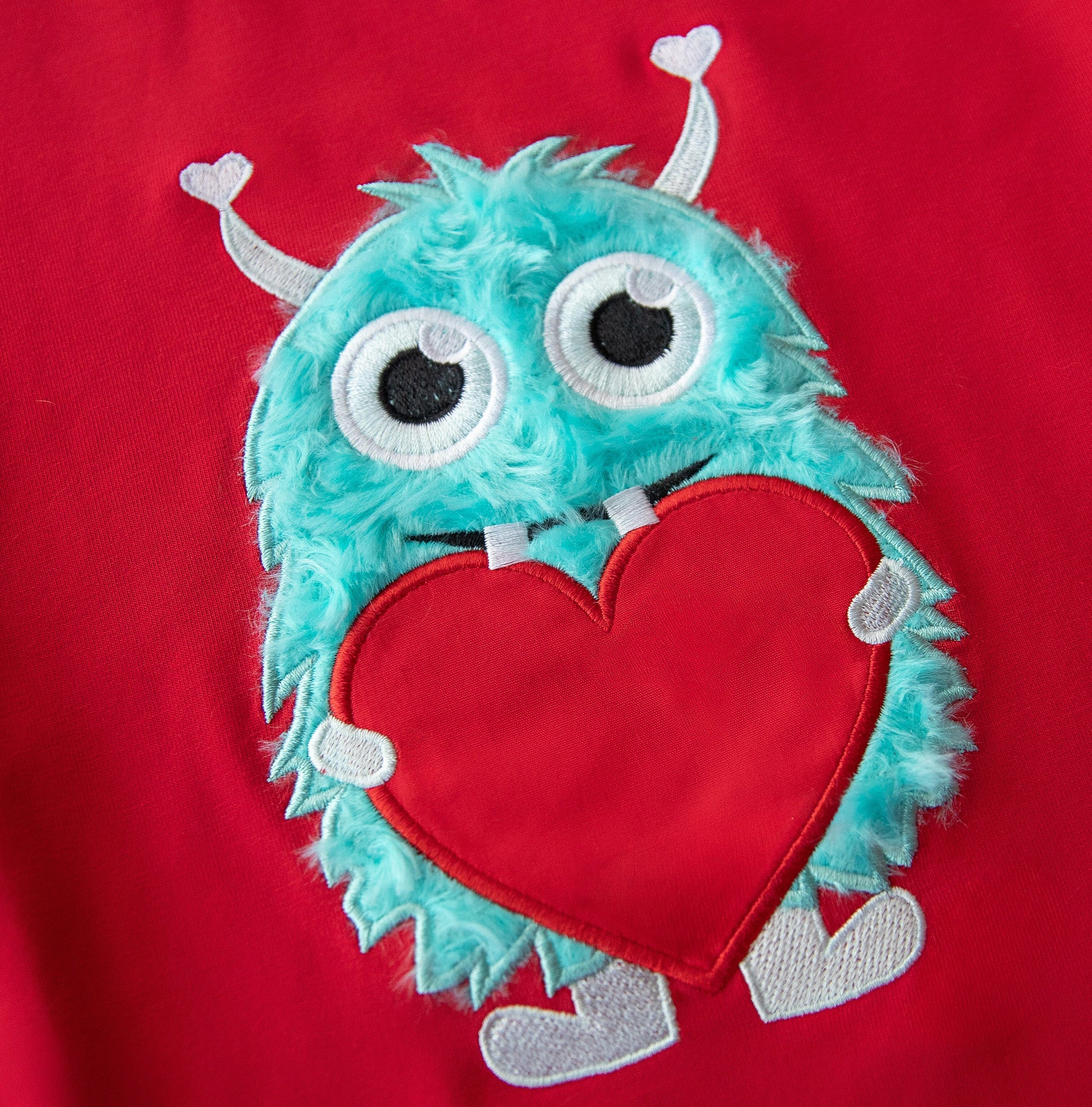 Red shirt with a turquoise monster holding a red heart on a red background